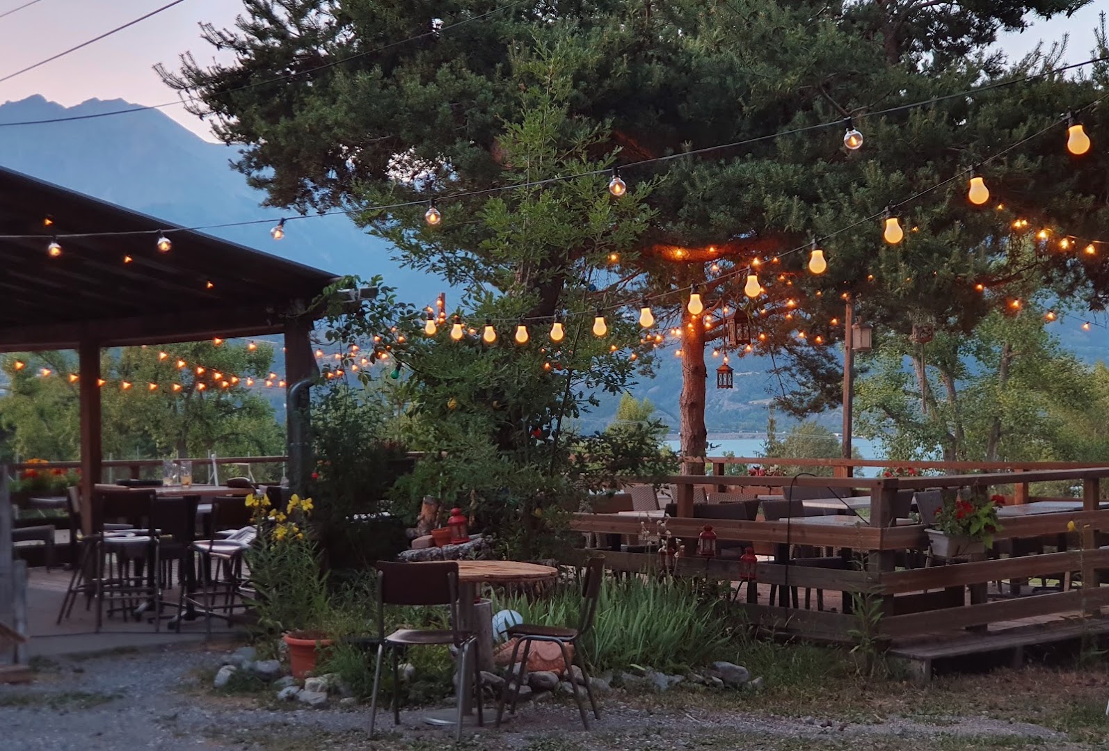 La terrasse du Pré d'Émeraude au coucher du soleil, les guirlandes illuminées face aux montagnes et au lac